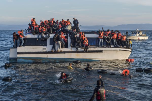 Migranti Barcone sovraccarico di migranti in mare aperto con giubbotti arancioni e motovedetta della guardia costiera.